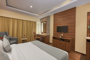 A hotel room with a bed, a desk, a chair, a television, and a mirror. - Southernstar Bangalore (Bengaluru)