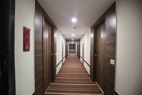 A hotel hallway with wooden doors, a striped carpet, and a red emergency equipment box. - Southernstar Bangalore (Bengaluru)