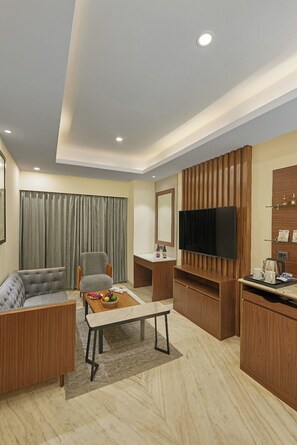 A modern living room with a sofa, armchair, coffee table, and a flat-screen TV mounted on a wooden wall. - Southernstar Bangalore (Bengaluru)