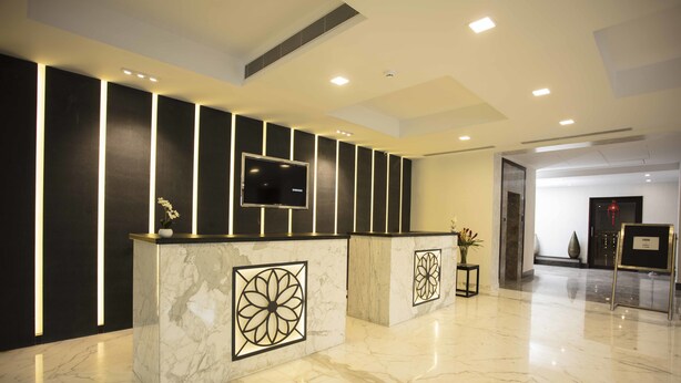 A modern reception area with marble flooring, a flat-screen TV, and a reception desk with a decorative panel. - Southernstar Bangalore (Bengaluru)
