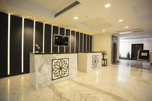 A modern reception area with marble flooring, a flat-screen TV, and a reception desk with a decorative panel. - Southernstar Bangalore (Bengaluru)