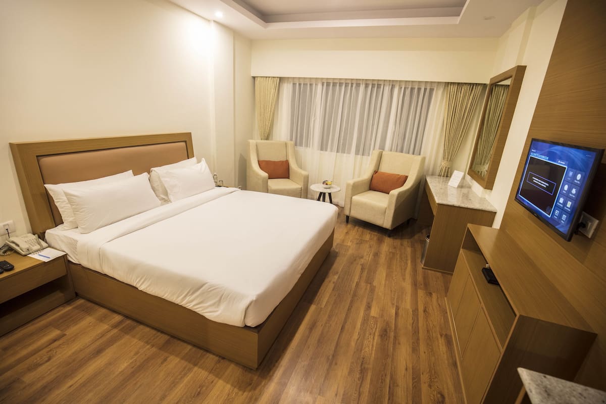 A hotel room with a large bed, two armchairs, a small table, a TV, and a wooden floor.