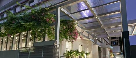 A modern building with a covered entrance, large windows, and potted plants.