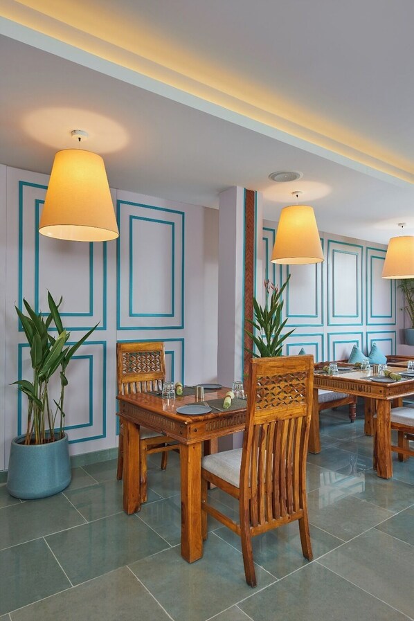A dining area with wooden tables and chairs, blue geometric wall patterns, and potted plants. - Southernstar Bangalore (Bengaluru)