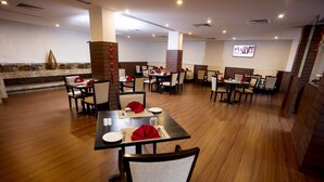 A restaurant with multiple tables and chairs, a television screen on the wall, and a decorative wall with a vase. - Southernstar Bangalore (Bengaluru)