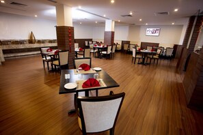 Un restaurante con varias mesas y sillas, una pantalla de televisión en la pared y una decoración que incluye un jarrón.