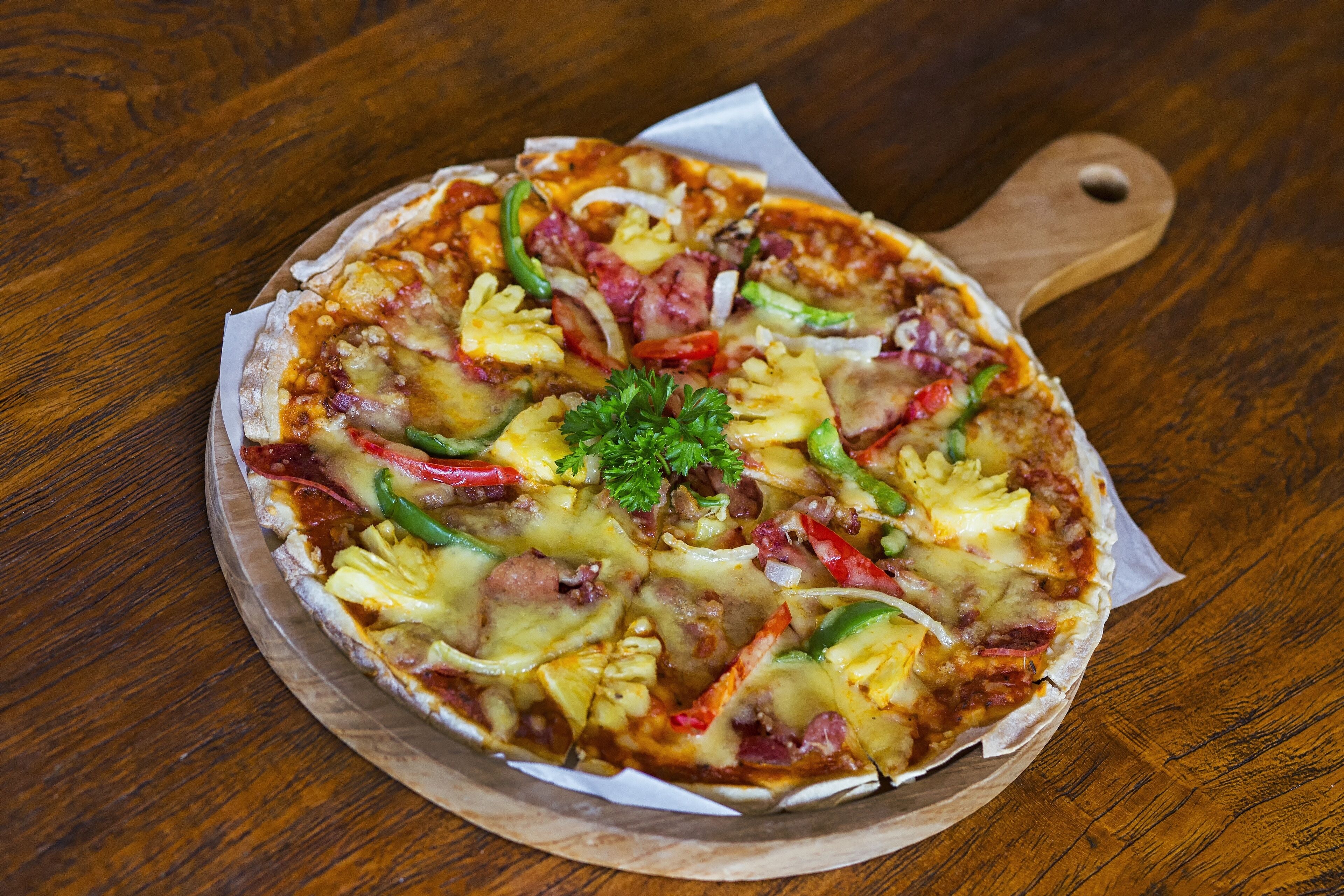 A pizza on a wooden board with a handle.