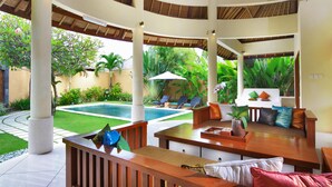A covered outdoor seating area with a pool in the background.