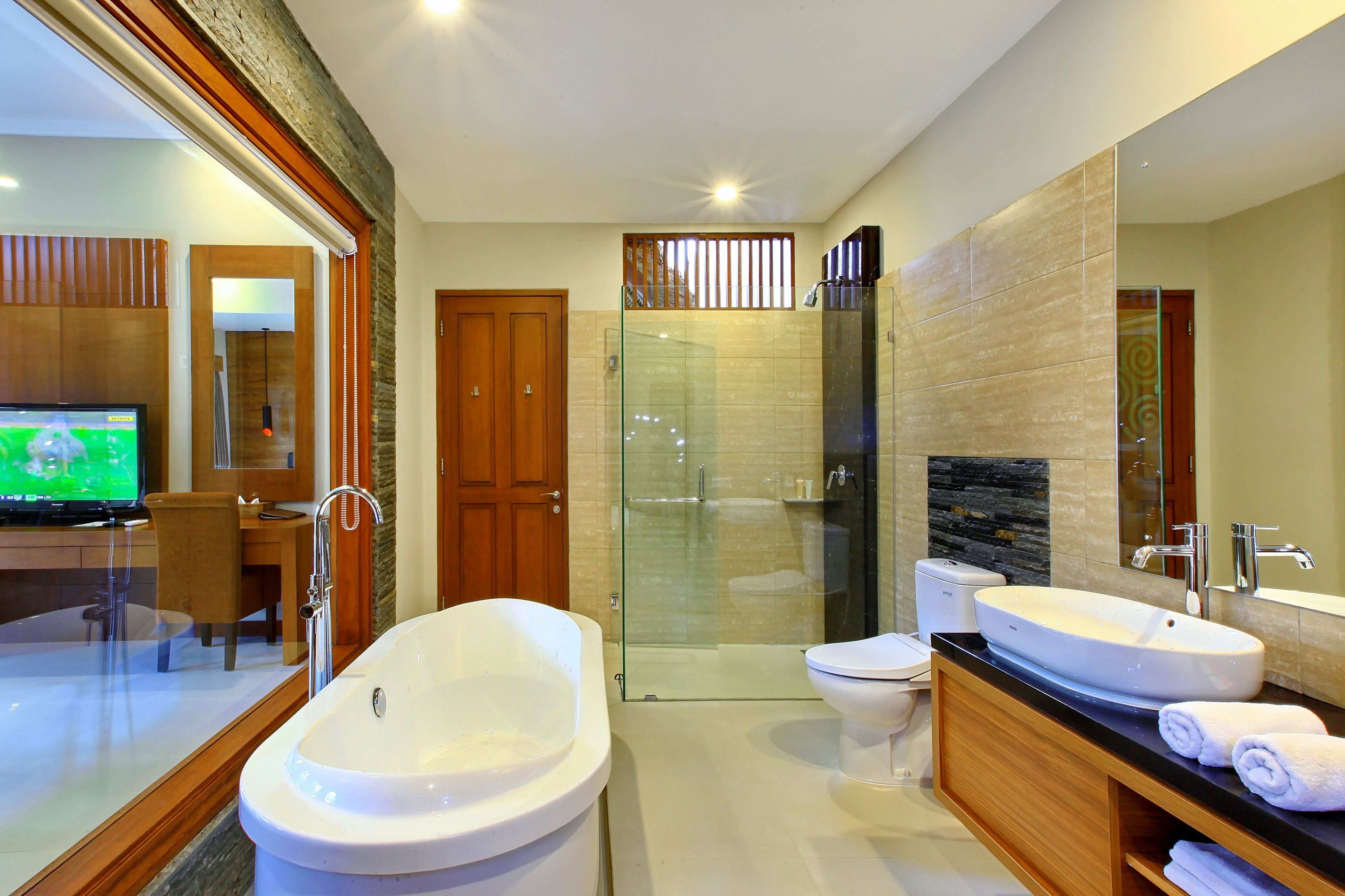 A modern bathroom with a large bathtub, a glass-enclosed shower, a toilet, and a vanity with a sink and mirror.