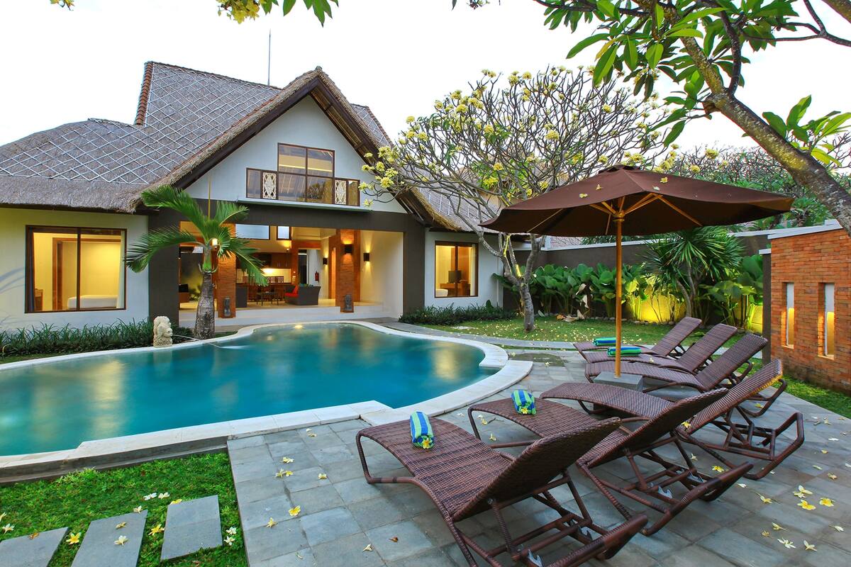 Una casa con piscina, sillas de descanso y un patio.