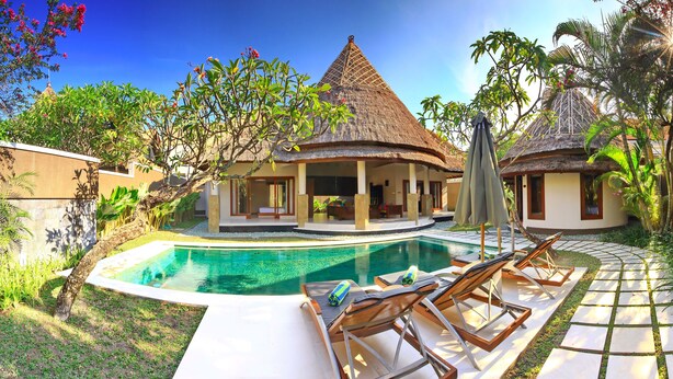 A resort with a swimming pool, lounge chairs, and thatched-roof buildings.