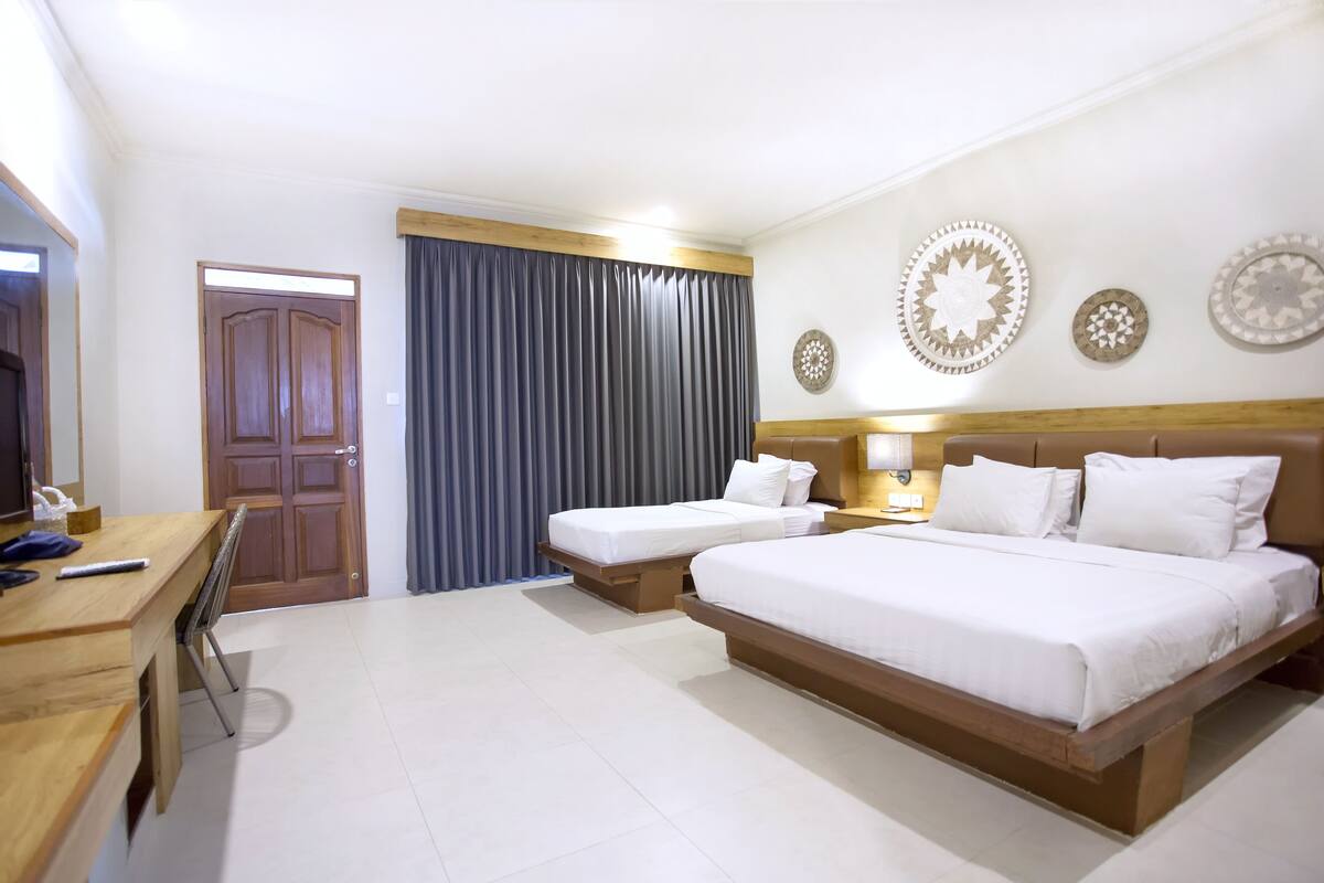 Habitación de hotel con dos camas individuales, un escritorio de madera, un televisor y un amplio ventanal con cortinas.