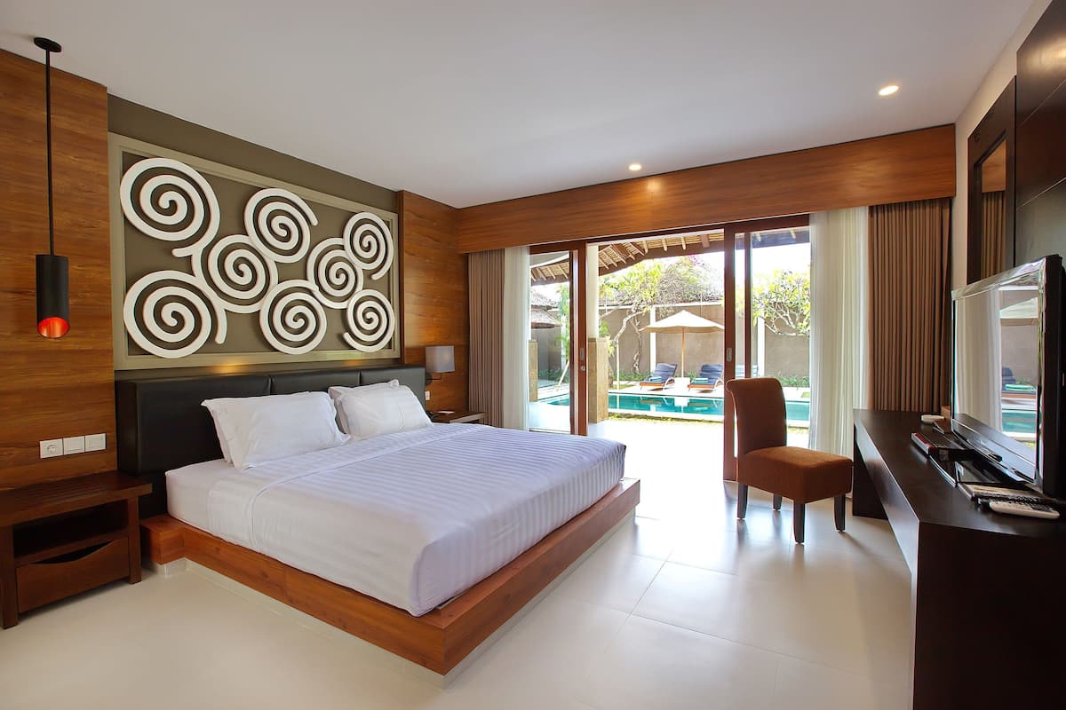 Una habitación de hotel moderna con una cama grande, un escritorio con televisor y vistas a una piscina al aire libre.