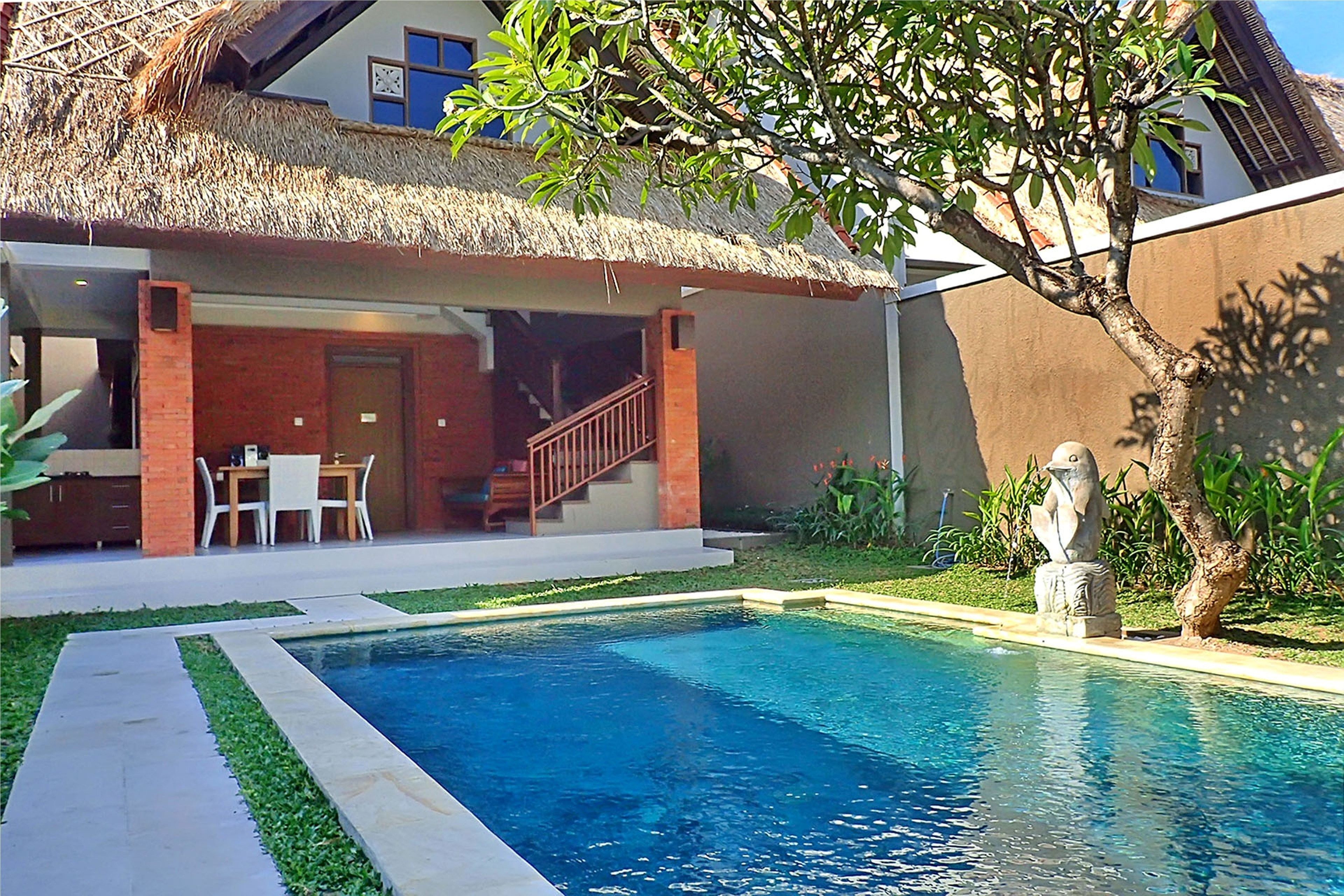 A swimming pool with a thatched-roof structure and a statue nearby.