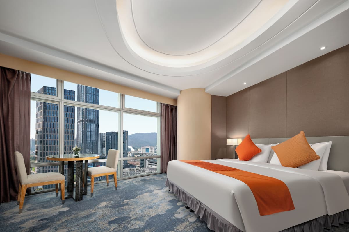 Een hotelkamer met een bed, twee stoelen, een ronde tafel en uitzicht op de stad.