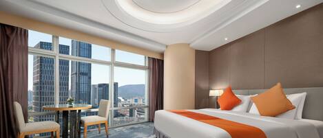 A hotel room with a bed, two chairs, a round table, and a city view.