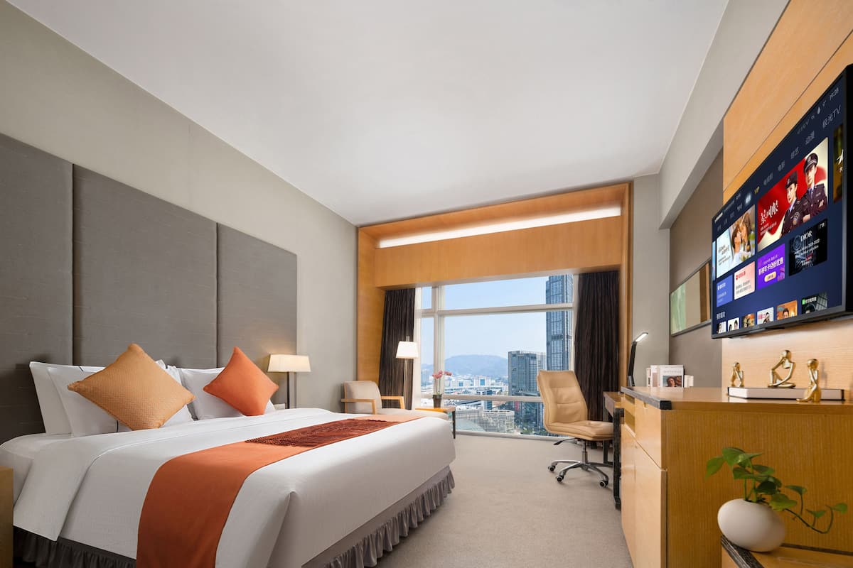 Een hotelkamer met een groot bed, een bureau met een computer en uitzicht op de stad.