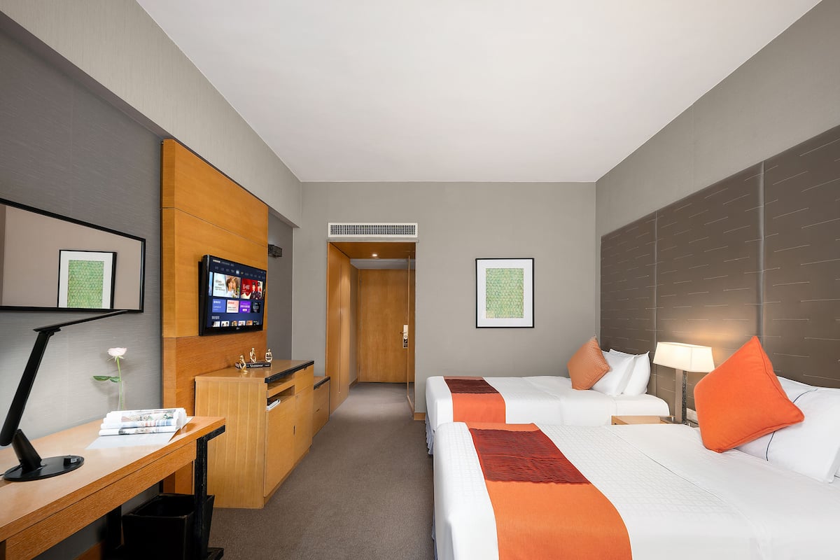 Een hotelkamer met twee bedden, een bureau, een televisie en een minibar.