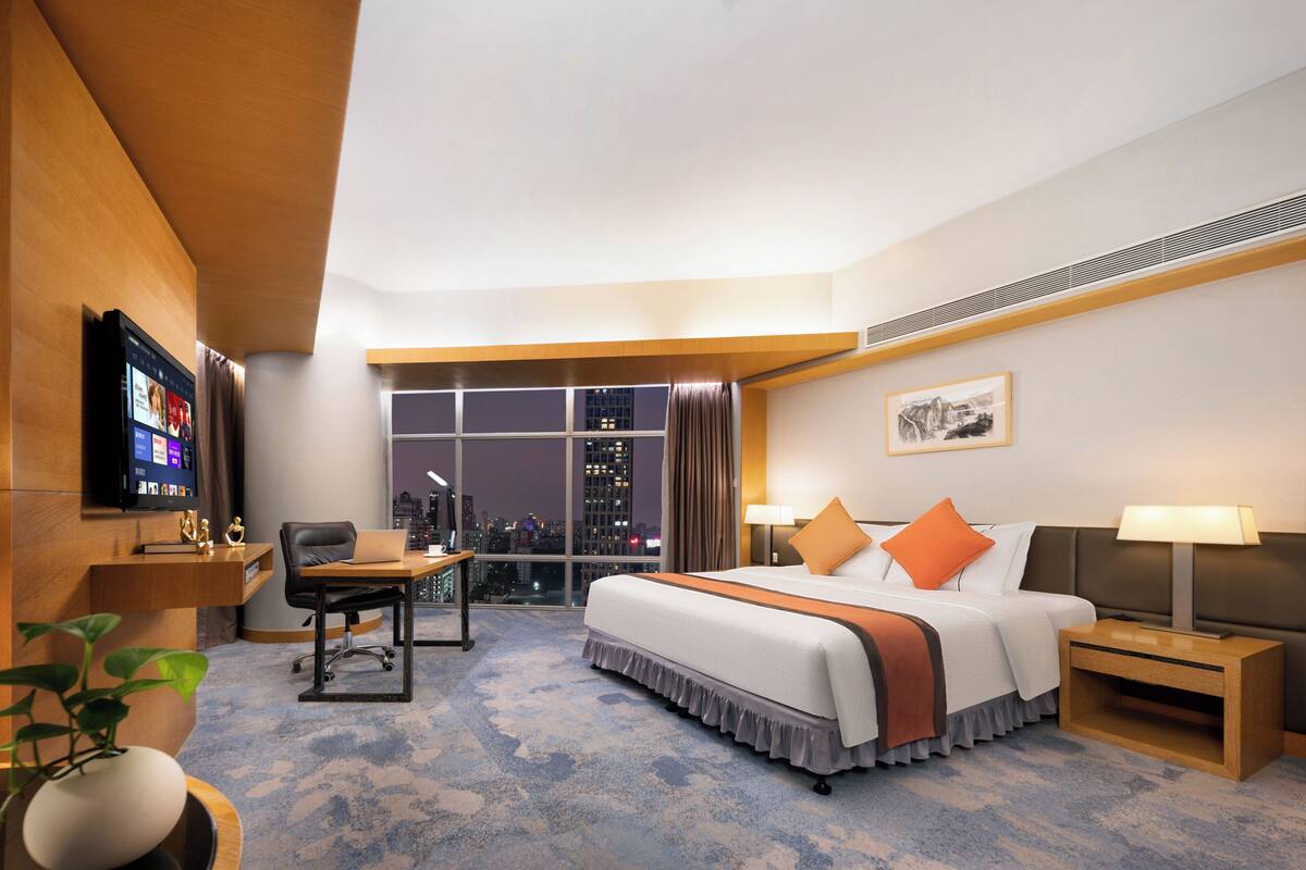 Een hotelkamer met een bed, bureau, stoel, televisie en uitzicht over de stad.