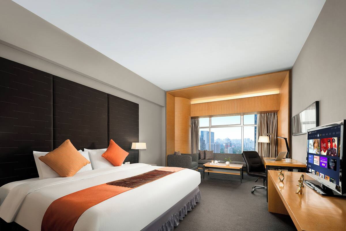 Een hotelkamer met een groot bed, een bureau, een stoel, een televisie en een raam met uitzicht op de stad.