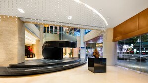 Eine moderne Lobby mit einer großen, schwarzen Skulptur, einer gewölbten Decke mit hängenden Leuchten und Blick auf die Straße.
