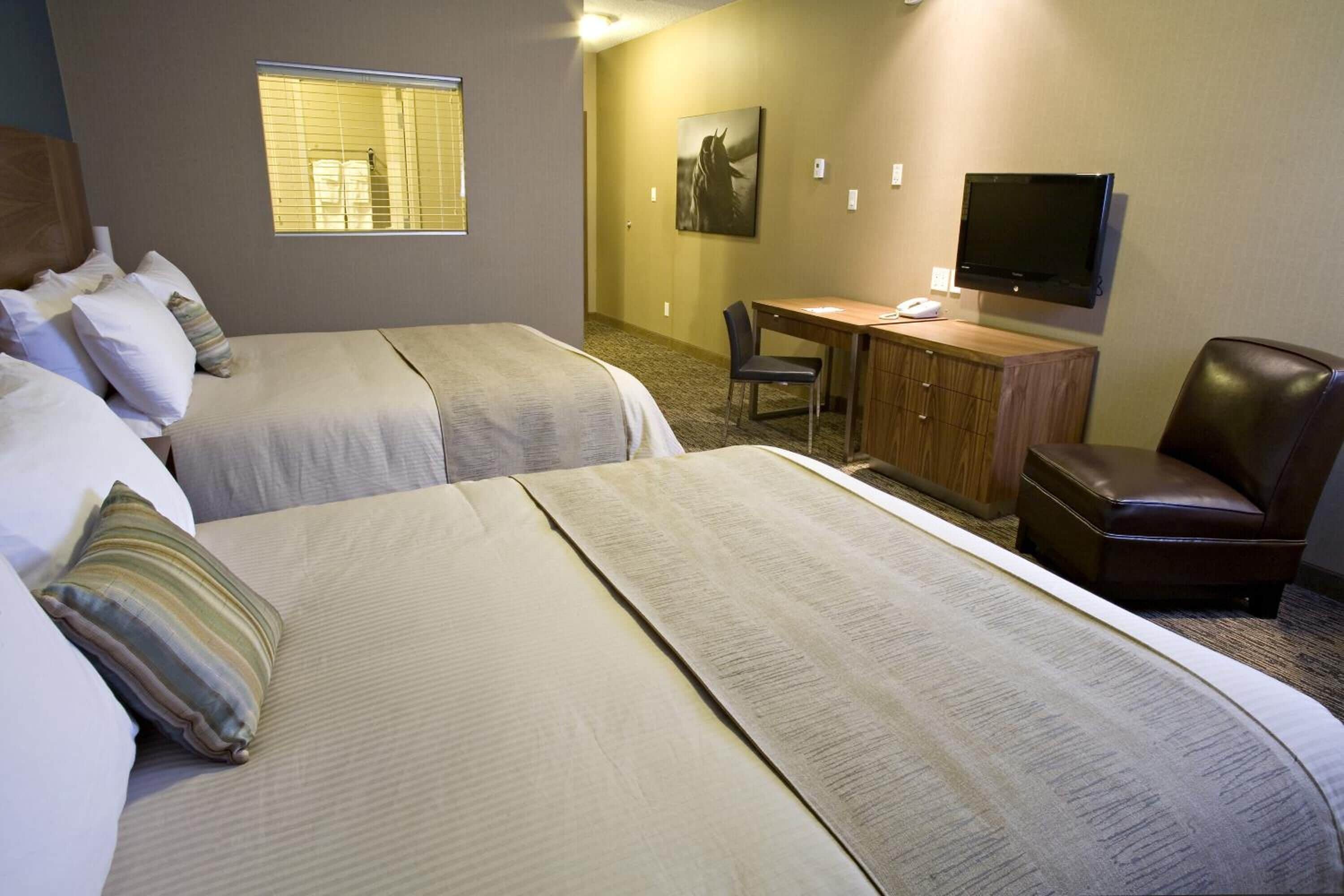 Ett hotellrum med två sängar, ett skrivbord, en stol, en tv och ett fönster.
