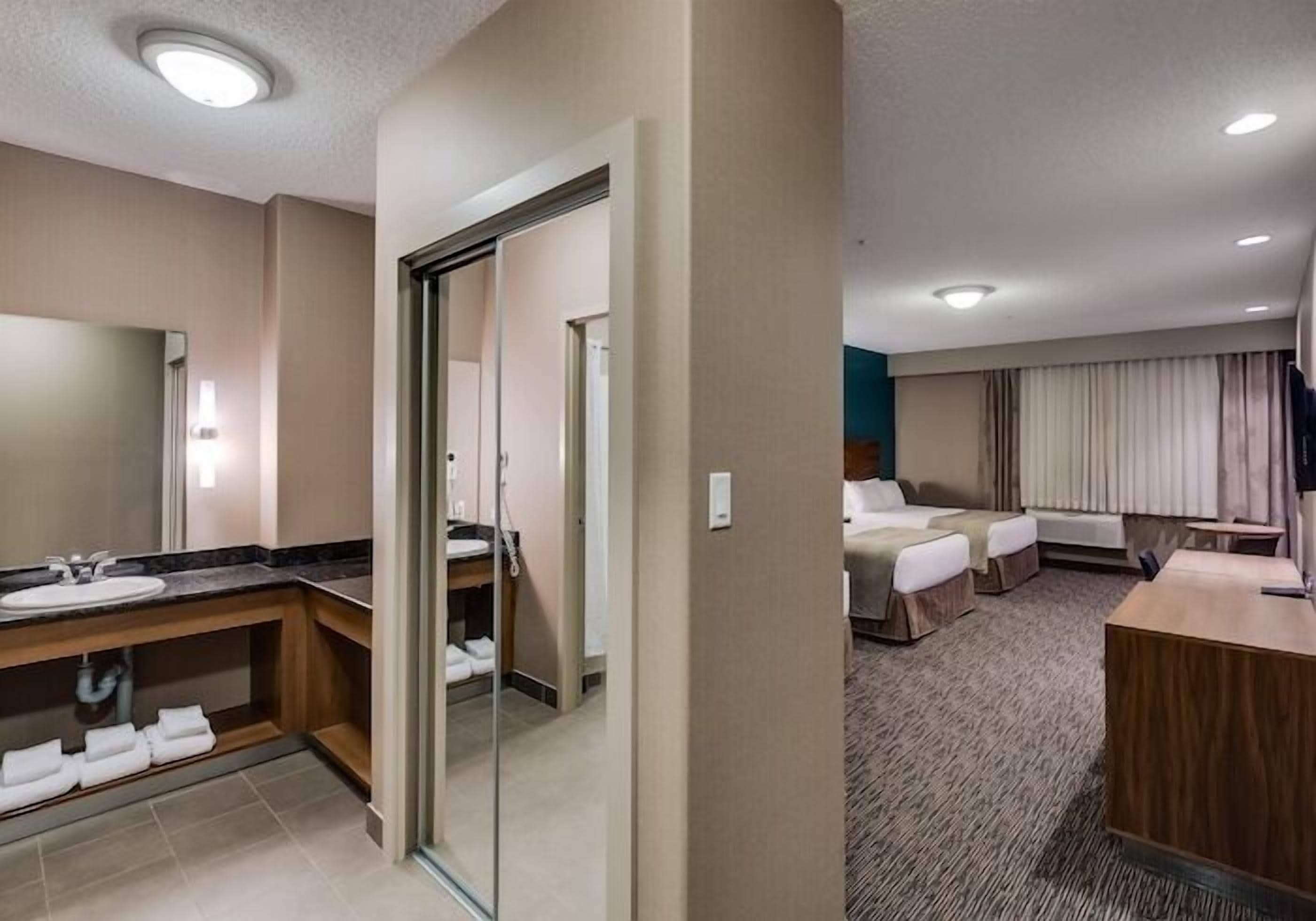 Una habitación de hotel con baño, cama, escritorio y un espejo grande.