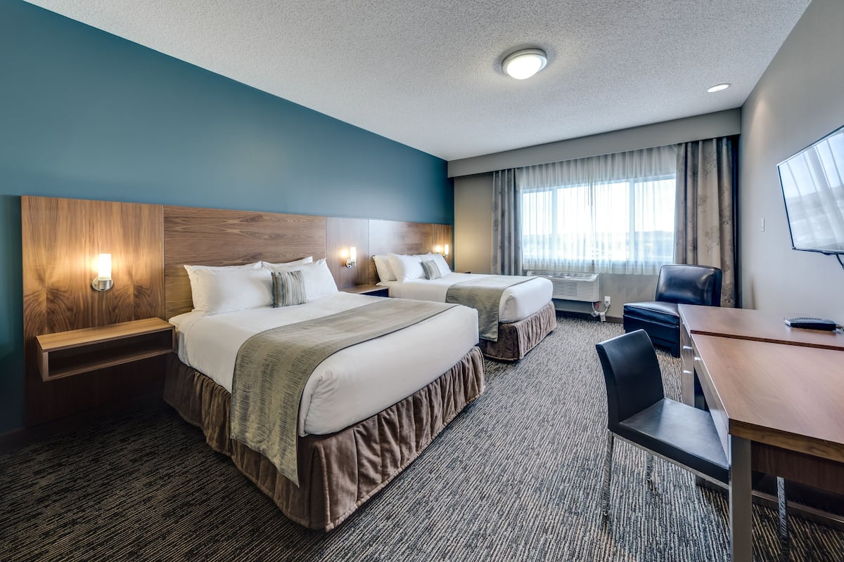A hotel room with two beds, a desk, a chair, and a TV.