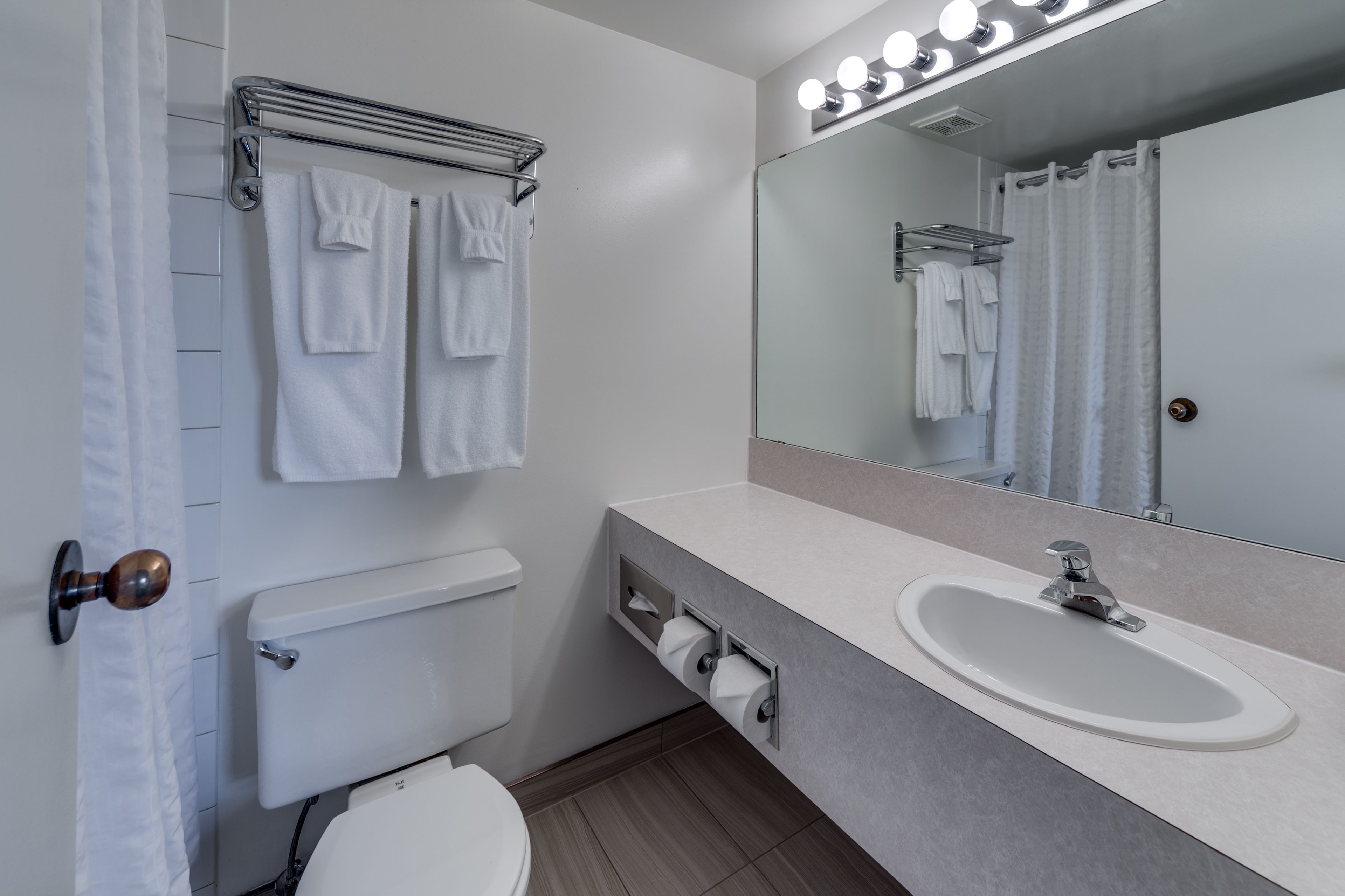 A modern bathroom with a white toilet, a sink with a mirror above it, and a towel rack with multiple towels.