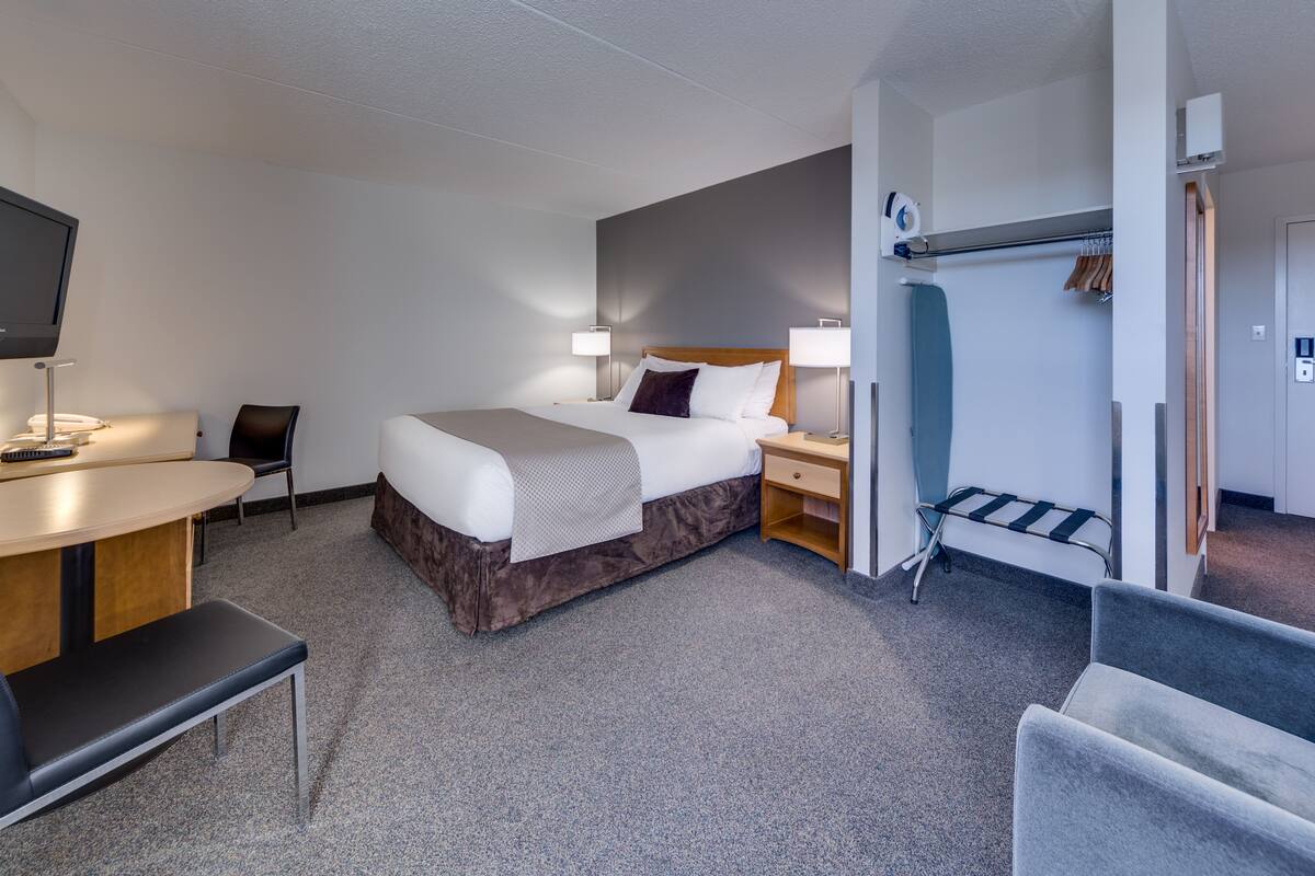 A hotel room with a bed, bedside tables, a desk, a chair, and a TV.