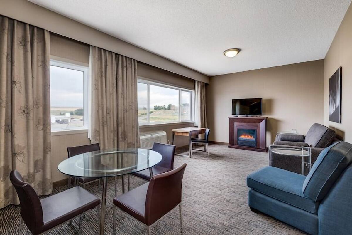 A hotel room with a glass dining table, a sofa, a fireplace, and a TV.