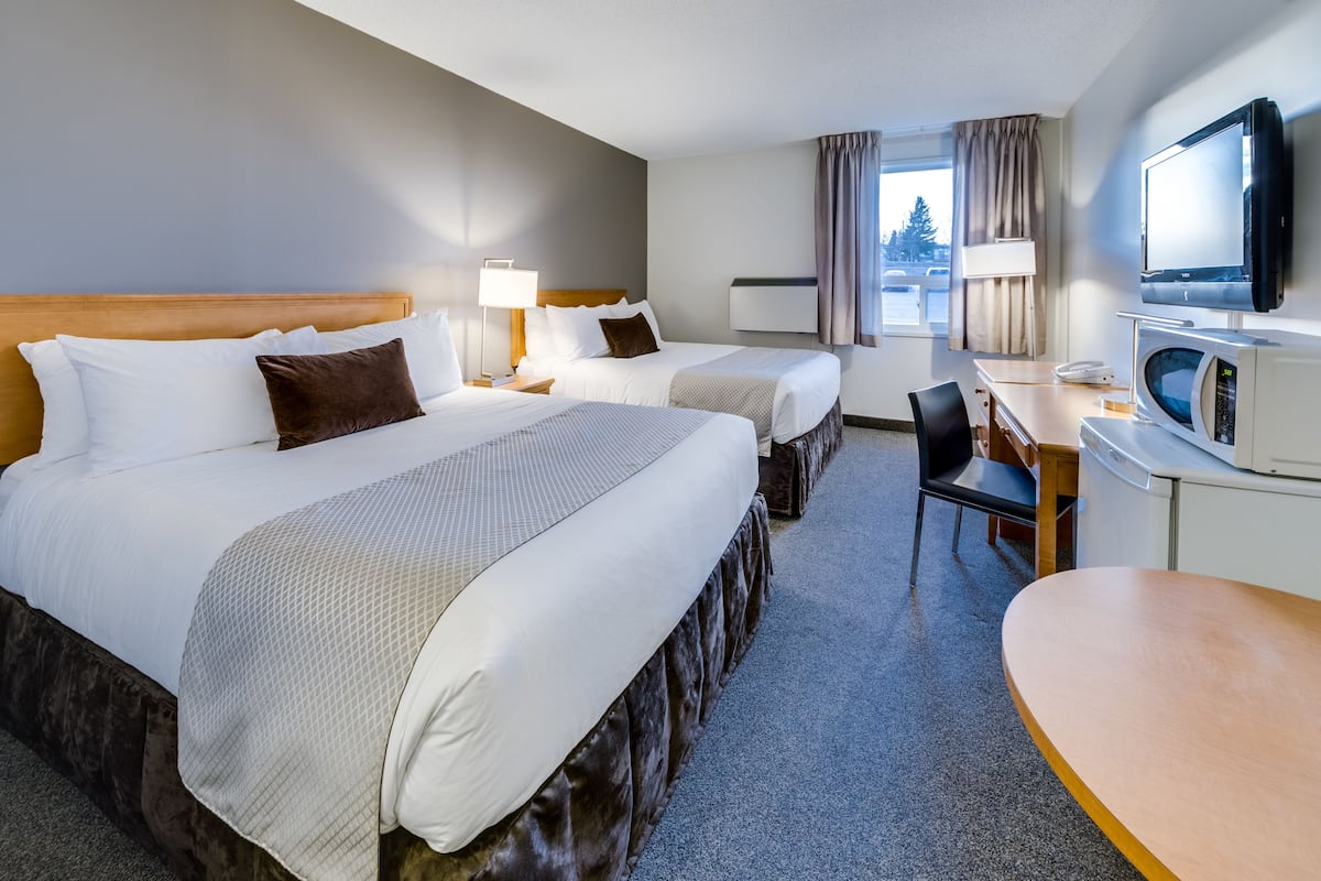 A hotel room with two beds, a desk, a chair, a TV, and a window with curtains.