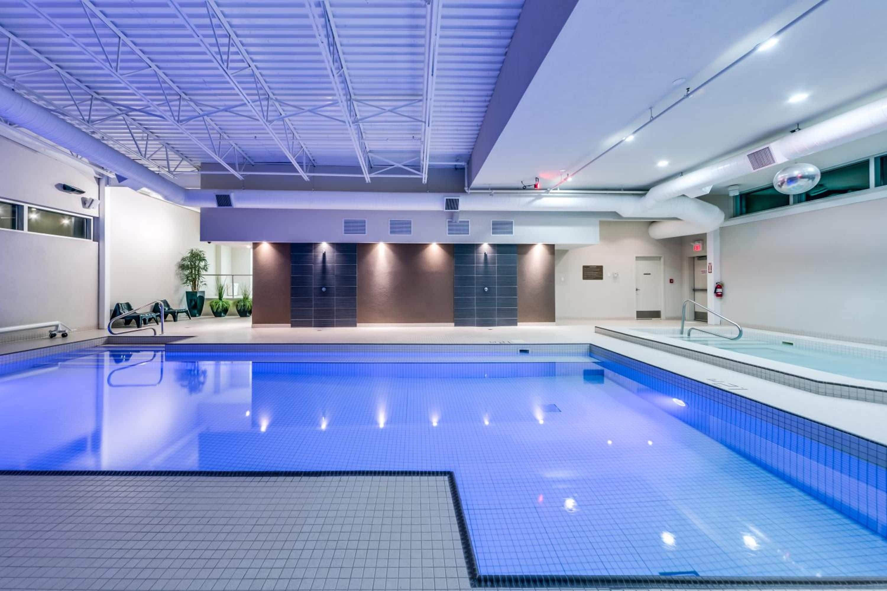 A large indoor swimming pool with clear blue tiles, a tiled floor, and a ceiling with a grid structure.