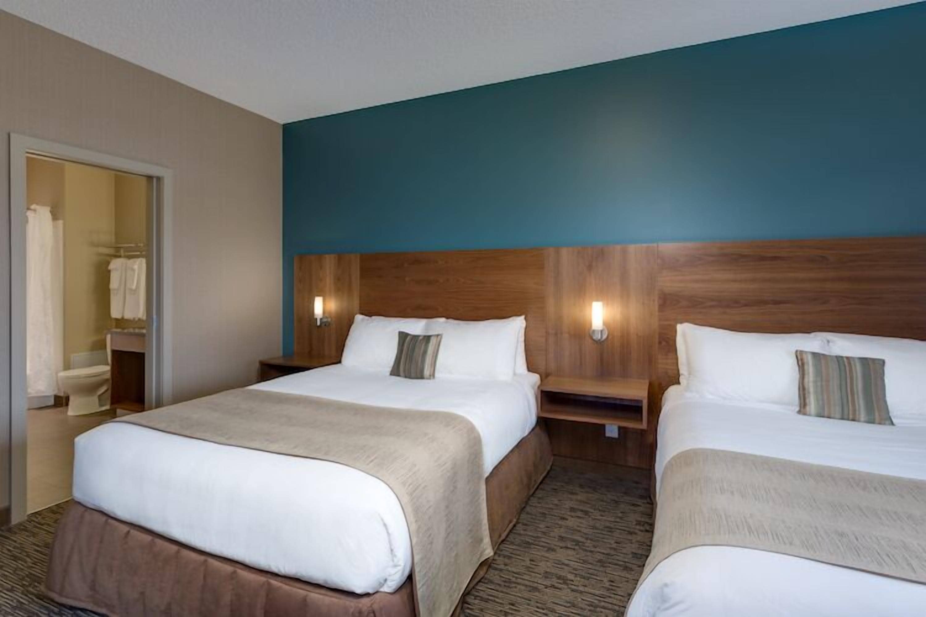 A hotel room with two beds, a wooden headboard, and a bathroom visible through an open door.