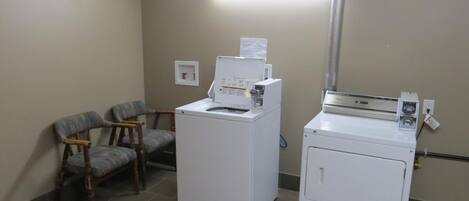 A laundry room with two washing machines, a chair, and a wall-mounted light fixture.