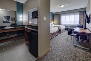 Habitación de hotel con kitchenette, una cama, un escritorio y un televisor.