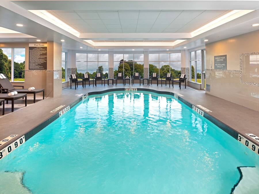 An indoor swimming pool with clear water, marked depth lines, and lounge chairs.