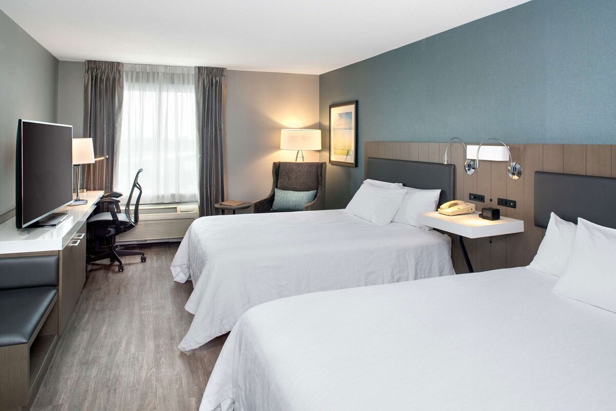 A hotel room with two beds, a desk with a TV, a chair, a lamp, and a bedside table with a phone.