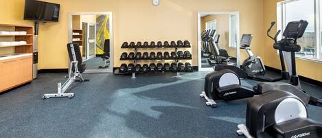 Un gimnasio con equipo de levantamiento de pesas, cintas de correr y mancuernas.
