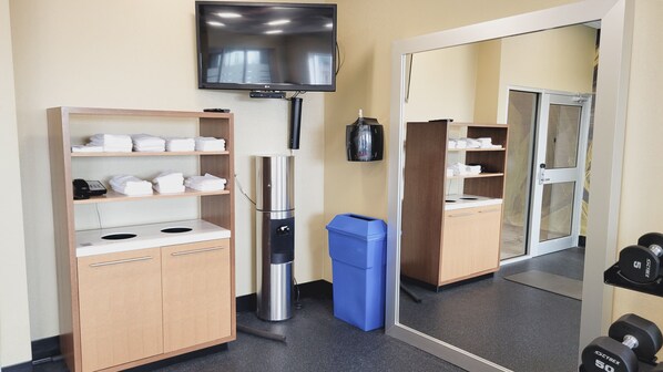 Habitación de hotel con televisor, minibar, espejo y un pequeño espacio para ejercitarse con mancuernas.