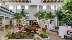 An indoor garden with a pond, wooden bridge, and tables set for dining. - Heritage Inn Hotel & Convention Centre Taber (Taber)