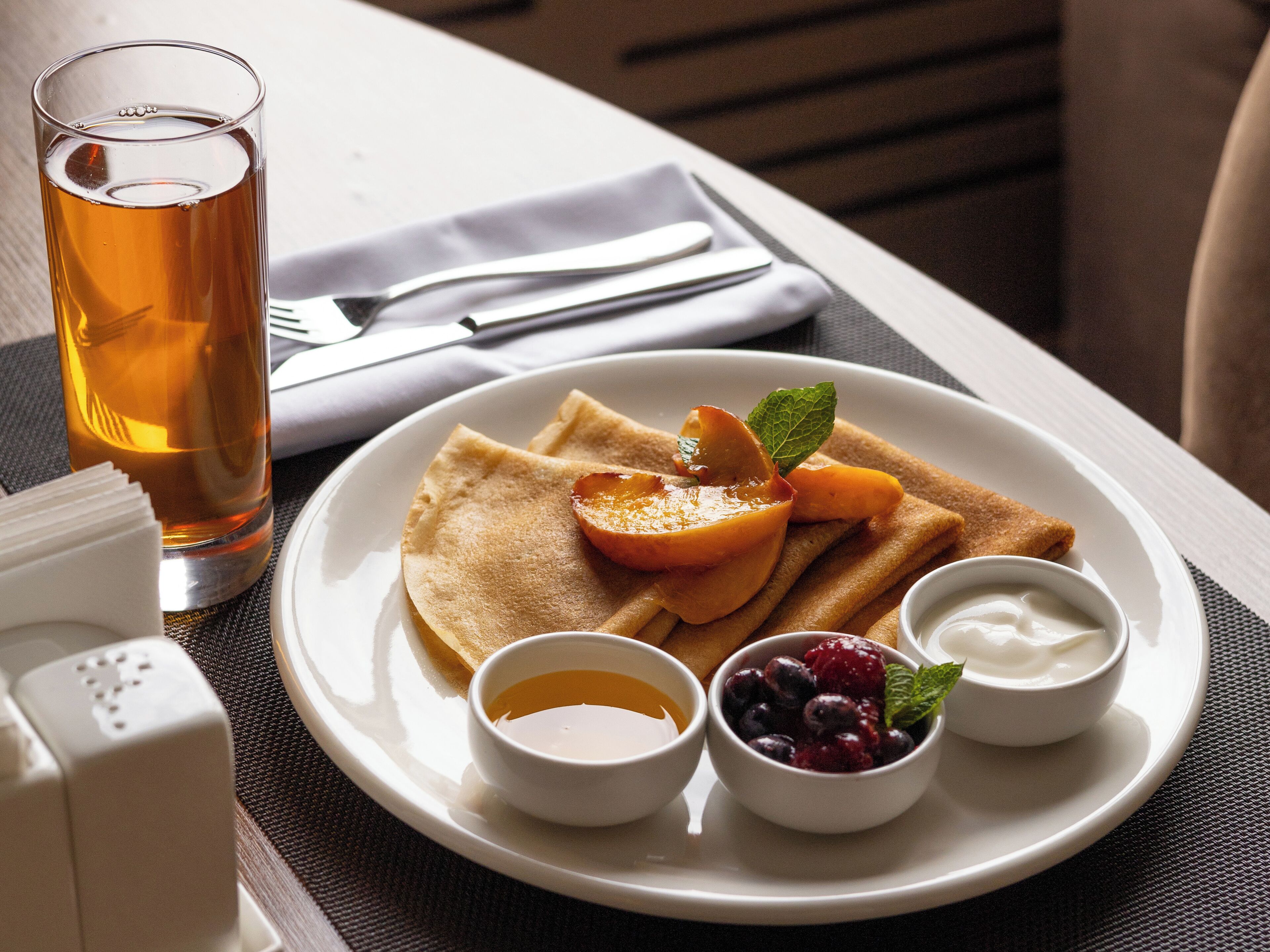 A plate with crepes, fruit, and two small bowls of cream.