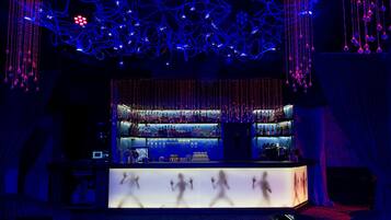 A bar area with a counter, shelves of bottles, and hanging lights.
