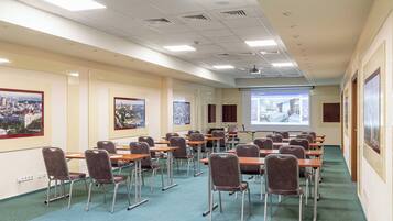 A conference room with rows of tables and chairs, a projector screen, and cityscape posters on the walls.