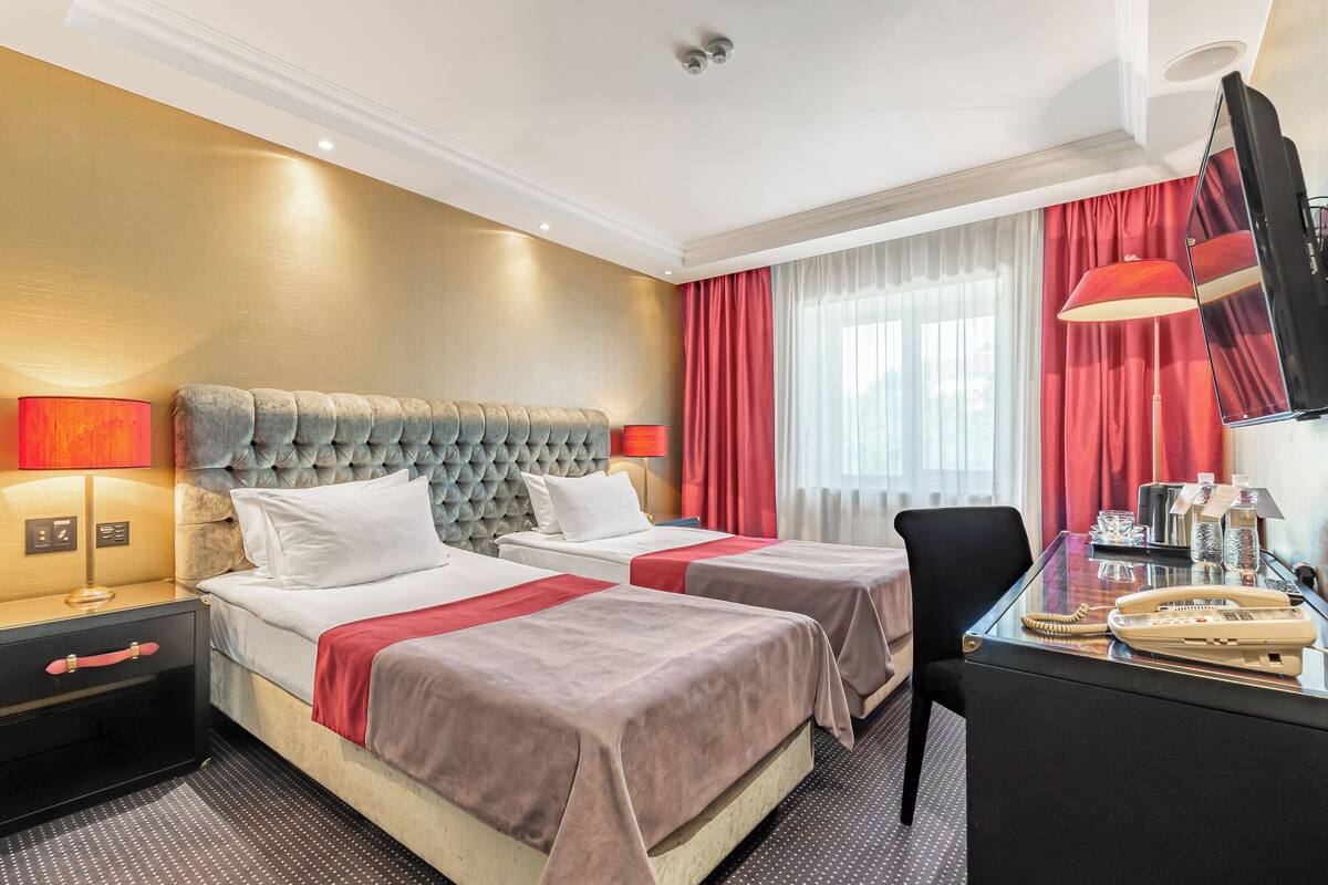 A hotel room with two beds, a desk with a telephone, and a TV.
