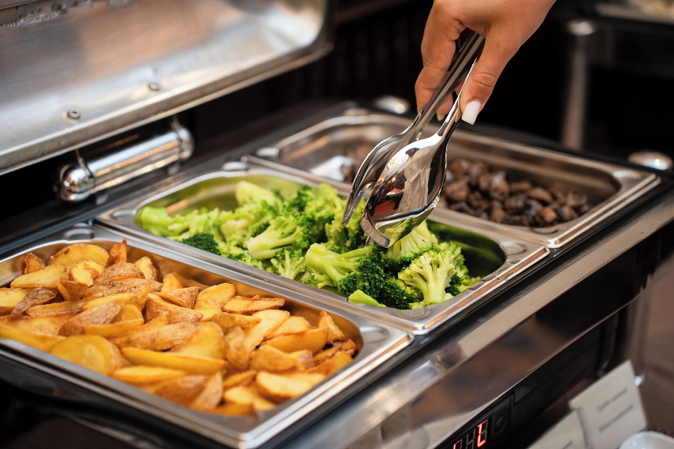 A buffet with trays of food including potatoes and broccoli.