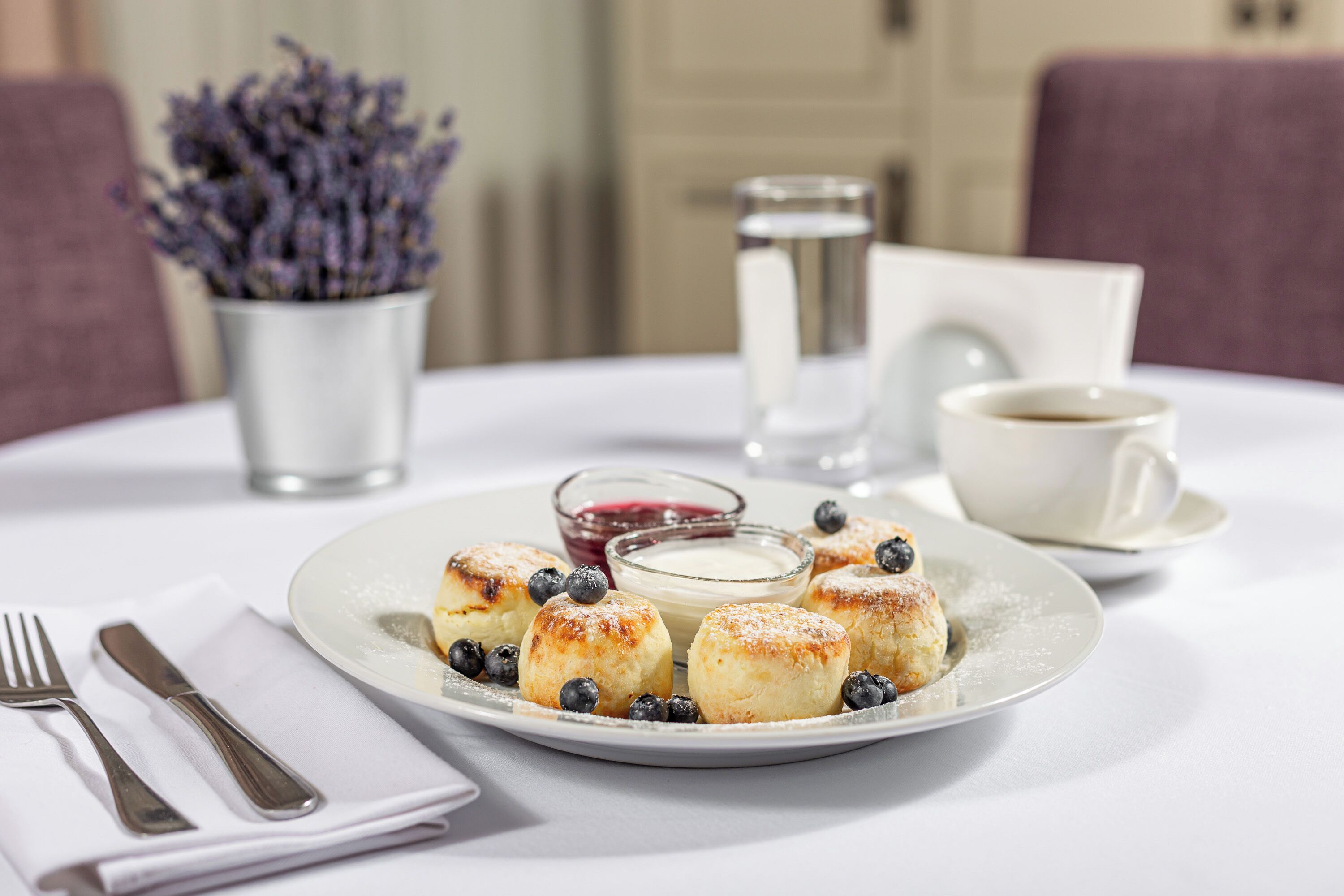 A plate of pastries with blueberries and a small bowl of cream on a white table.