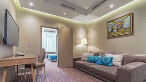 Et hotelværelse med seng, skrivebord, stol, sofa, lampe og et billede på væggen.
