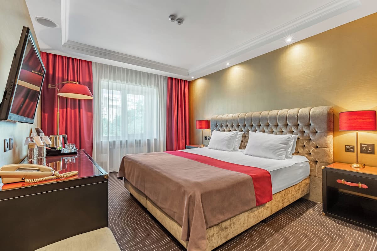 A hotel room with a large bed, a desk with a mirror, a lamp, and a nightstand.
