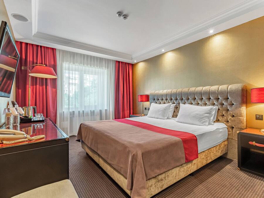 Habitación de hotel con una cama grande, un escritorio con espejo, una lámpara y una mesita de noche.